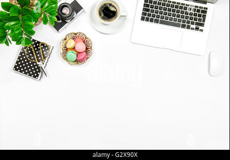 Creativi sul posto di lavoro femminile. Caffè, amaretto cookies, computer portatile e pianta verde su bianco sfondo tabella Foto Stock