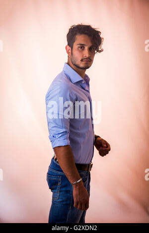 Ritratto di bruna giovane uomo alla luce maglietta blu e jeans, stando in piedi in studio shot contro uno sfondo chiaro Foto Stock