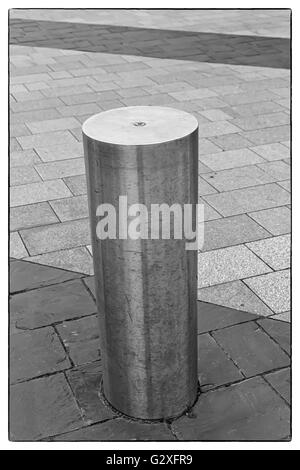 Foto in bianco e nero di un acciaio inossidabile bollard sul marciapiede grigio con poche righe di colore grigio scuro di lastre per pavimentazione con un vintage bo Foto Stock