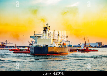 Grande nave con la scorta rimorchiatori partenza dal porto al tramonto. Foto Stock