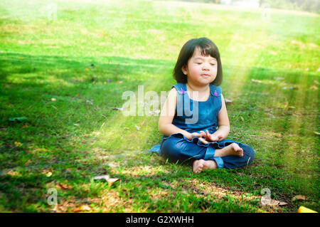 Poco ragazza asiatica la pratica di mindfulness meditazione all'aperto in un parco. Foto Stock