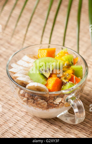 Colazione dietetica. Muesli, yogurt, frutta tropicale: mango, kiwi, ananas, frutto della passione in coppa su un sfondo di paglia Foto Stock