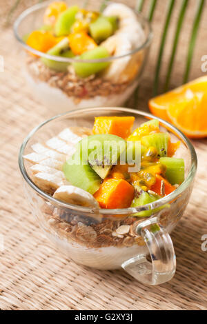 Colazione dietetica. Muesli, yogurt, frutta tropicale: mango, kiwi, ananas, frutto della passione in coppa su un sfondo di paglia Foto Stock