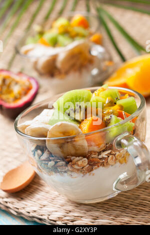 Colazione dietetica. Muesli, yogurt, frutta tropicale: mango, kiwi, ananas, frutto della passione in coppa su un sfondo di paglia Foto Stock