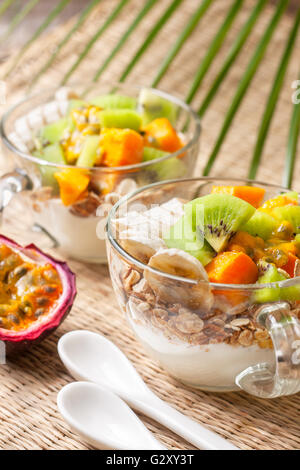 Colazione dietetica. Muesli, yogurt, frutta tropicale: mango, kiwi, ananas, frutto della passione in coppa su un sfondo di paglia Foto Stock