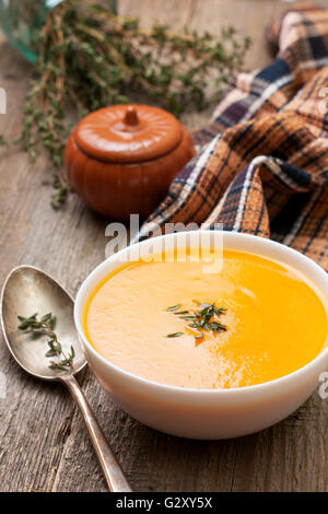 Zuppa di zucca - la purea in una ciotola bianco, un vecchio cucchiaio, igienico, timo su un vecchio sfondo di legno Foto Stock