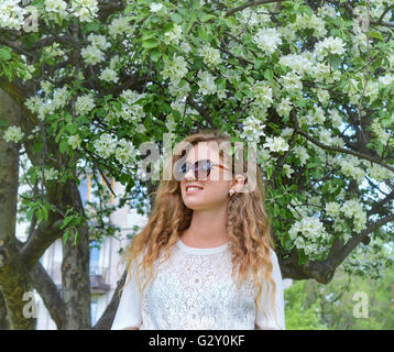 Una ragazza sorridente ad una fioritura del melo in un giardino in primavera. Foto Stock