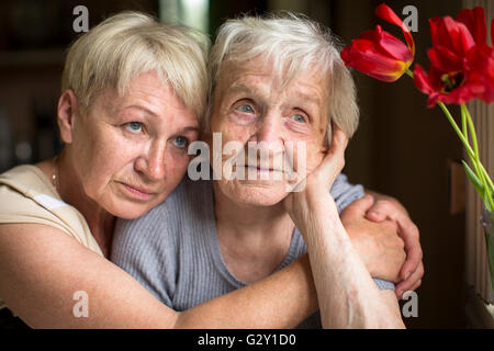 Una donna anziana seduta in un abbraccio con la sua figlia adulta. Foto Stock