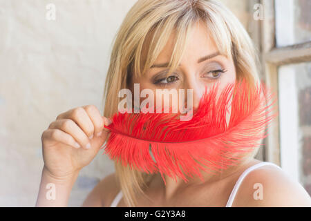 Giovane donna nasconde il viso con un red feather Foto Stock