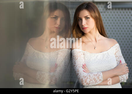 La riflessione di una giovane donna le braccia incrociate appoggiata contro il muro Foto Stock