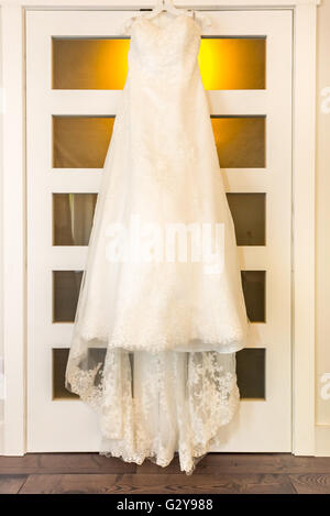 Abito da sposa appeso su una porta in camera calda luce. Un abito da sposa si blocca su una camera da letto porta armadio in camera calda luce. Foto Stock