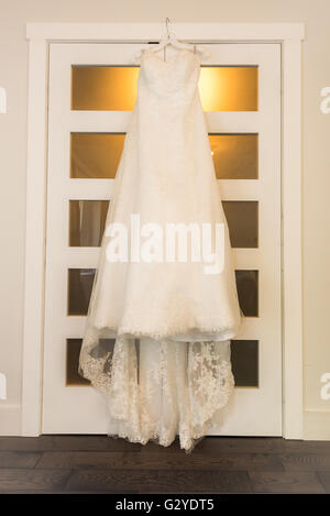 Abito da sposa appeso su una porta in camera calda luce. Un abito da sposa si blocca su una camera da letto porta armadio in camera calda luce. Foto Stock