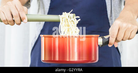 Uomo asiatico cucinare gli spaghetti in pentola rosso Foto Stock