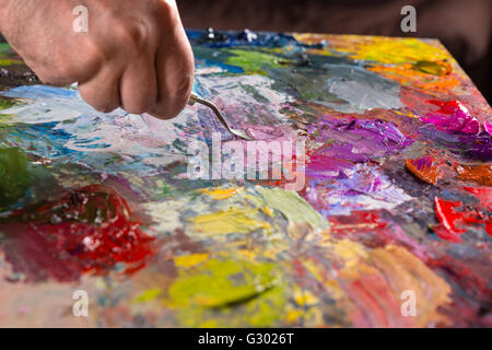 Professional coltello tavolozza mescolando vari colori luminosi sulla tavolozza colorata in un studio Foto Stock