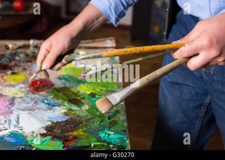 Artista maschile mano azienda pallete khife e pennelli sotto la palette colorate nel suo studio Foto Stock