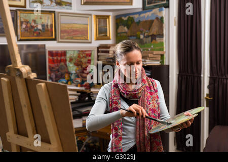 Professional artista femminile ottenere pronto per la verniciatura in una galleria tenendo un coloratissimo artisti tavolozza e pennello in mano Foto Stock