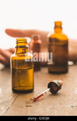 Bottiglie di medici e la pipetta contenente fluido tossico con la mano di una vittima di un reato nel retro Foto Stock
