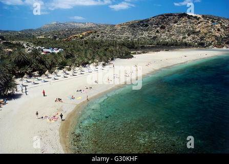 La Grecia e le isole greche, Creta, Vai, i visitatori a prendere il sole sulla spiaggia che si affaccia traslucido acque blu del mare, con sfondo di wild Palm grove Foto Stock