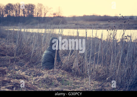 Traveler si siede in un campo rurale e godere il paesaggio. Lonely Man a guardare oltre la foschia mattutina il panorama su sunrise Foto Stock