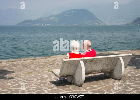 Coppia di anziani seduti al sole su una panchina nel parco in Iseo sulle rive del lago d'Iseo, Lombardia, Italia Foto Stock
