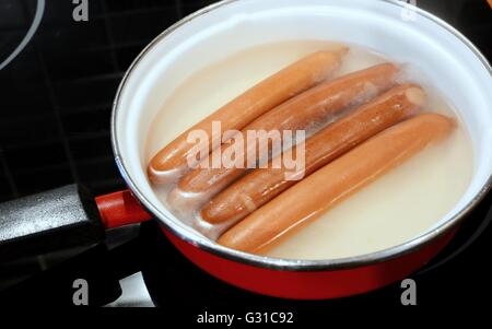 Quattro salsicce (frankfurter wurst) con punto di ebollizione in acqua calda nella teglia. Bollire frankfurters. Foto Stock