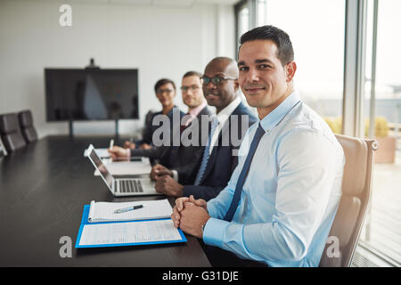 Multirazziale executive business team in un incontro seduti a una conferenza aziendale tabella con la messa a fuoco per un uomo ispanico in avanti Foto Stock