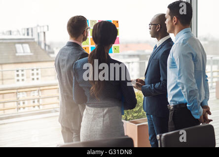 Quattro diversi imprenditori e multirazziale in piedi in un gruppo nella parte anteriore di un alta finestra chiave guardando una serie di coloratissimi memo stu Foto Stock