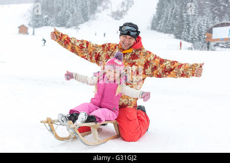 Padre e figlia in posa seduta su una slitta in inverno Foto Stock