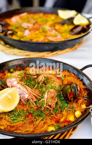 Primo piano di una fideua spagnola, un tipico tagliatelle casseruola con frutti di mare, in una padella per paella su un set di tavolo e una paella in backgr Foto Stock