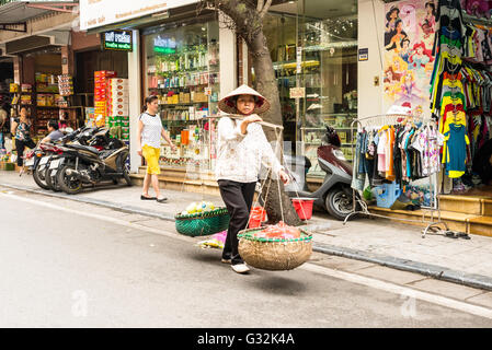 Venditore ambulante che trasportano la frutta e la verdura in cesti usando un palo portante, chiamato anche un polo di spalla in Hanoi Foto Stock