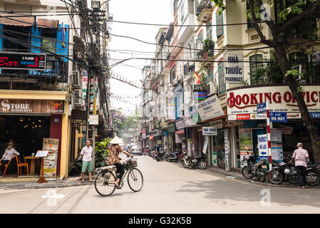 La donna che indossa il tradizionale vietnamita hat escursioni in bicicletta in una strada della città vecchia di Hanoi e. Foto Stock