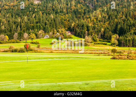 Un foro di golf con una bandiera rossa pole su una bella vivace Campo da golf Foto Stock