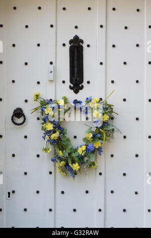 Molla di cuore floreale corona su un di legno bianco porta chiodati. Cotswolds, Inghilterra Foto Stock