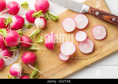 Ravanelli freschi sulla vecchia scheda di taglio con il coltello. Rossa affettata ravanelli. Foto Stock