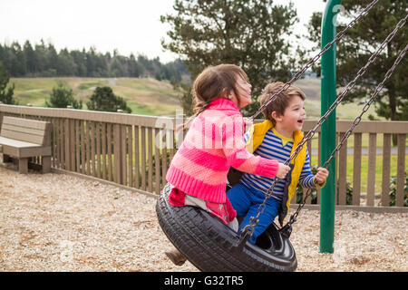 Un ragazzo e una ragazza seduta sulla rotazione dei pneumatici nel parco giochi Foto Stock