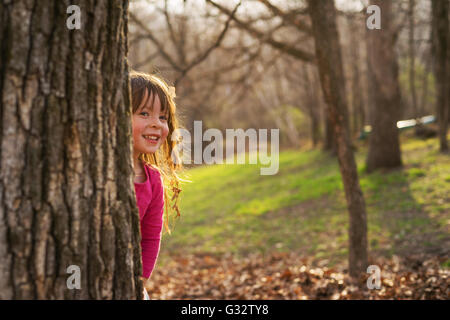 Ragazza sorridente nascondendo dietro ad un albero nel parco Foto Stock