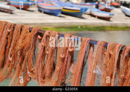 Il pittoresco red reti da pesca appesa ad asciugare e barche colorate in background nel porto di Mindello, Sicilia Foto Stock