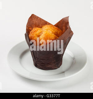 Deliziosa torta di muffin in carta marrone sulla piastra su sfondo bianco. Chiudere fino in vista laterale. Foto Stock