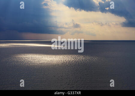 Nuvoloso seascape dopo tempesta vedendo naturale di raggi di sole al tramonto. Raggi di sole che splende attraverso le nuvole e riflessa in nero se Foto Stock