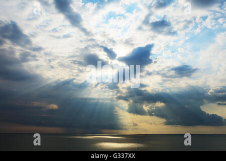 Nuvoloso seascape dopo tempesta vedendo naturale di raggi di sole al tramonto. Raggi di sole che splende attraverso le nuvole e riflessa in nero se Foto Stock