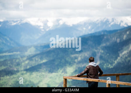 Giovane uomo in cerca del cofano sul paesaggio di montagna dal molo in legno al mattino. Vista posteriore foto Foto Stock