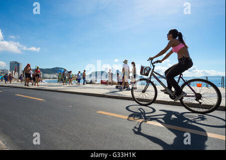 RIO DE JANEIRO - MARZO 20, 2016: Una donna brasiliana cavalca una bicicletta sulla spiaggia Avenida Atlântica pista ciclabile lungomare. Foto Stock