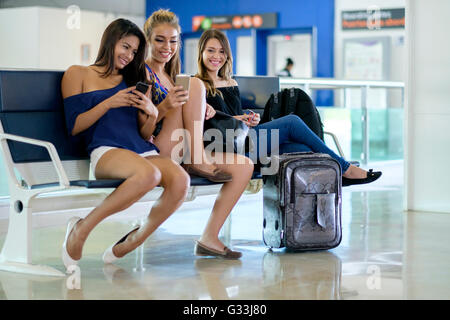 Gruppo di 3 giovani donne seduta sul banco a terminale di un aeroporto in attesa del volo di coincidenza Foto Stock