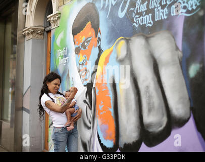 Mona Morrison con il suo bambino di 9 mesi, figlia Reniah guardando un graffito murale del boxer Muhammad Ali, a Camberwell, Londra Sud, come attore Will Smith e ex World Heavyweight Boxing champion Lennox Lewis sarà pallbearers a Muhammad Ali i funerali, è stato annunciato. Foto Stock