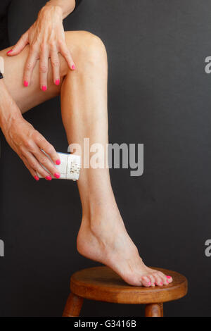 Una donna la rasatura le gambe tirando la pelle con le mani e mettere il piede sullo sgabello Foto Stock