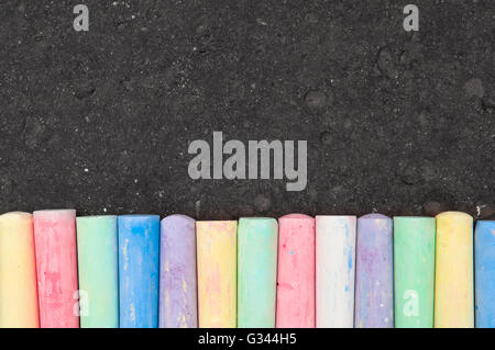 Pastello colorato sidewalk chalk su asfalto scuro dello sfondo. Vista superiore Foto Stock