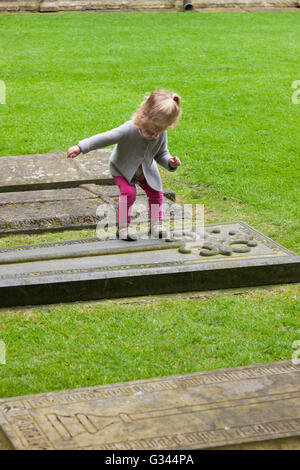 Bambino / bambini / Kids / kid esplora intorno tombe nel chiostro Garth / chiostri giardino presso la Cattedrale di Lincoln, Lincoln. Regno Unito. Foto Stock