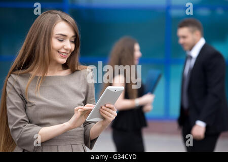 Ritratto di fiducioso giovane donna che guarda la schermata di tablet con felice espressione facciale all'esterno. Successo caucasico bello Foto Stock
