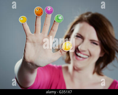 Sorridente giovane donna con faccina sorridente figurine sulle sue dita Foto Stock