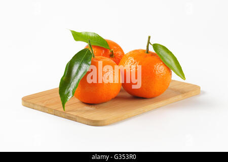 Tre i tangerini con foglie sul tagliere di legno Foto Stock